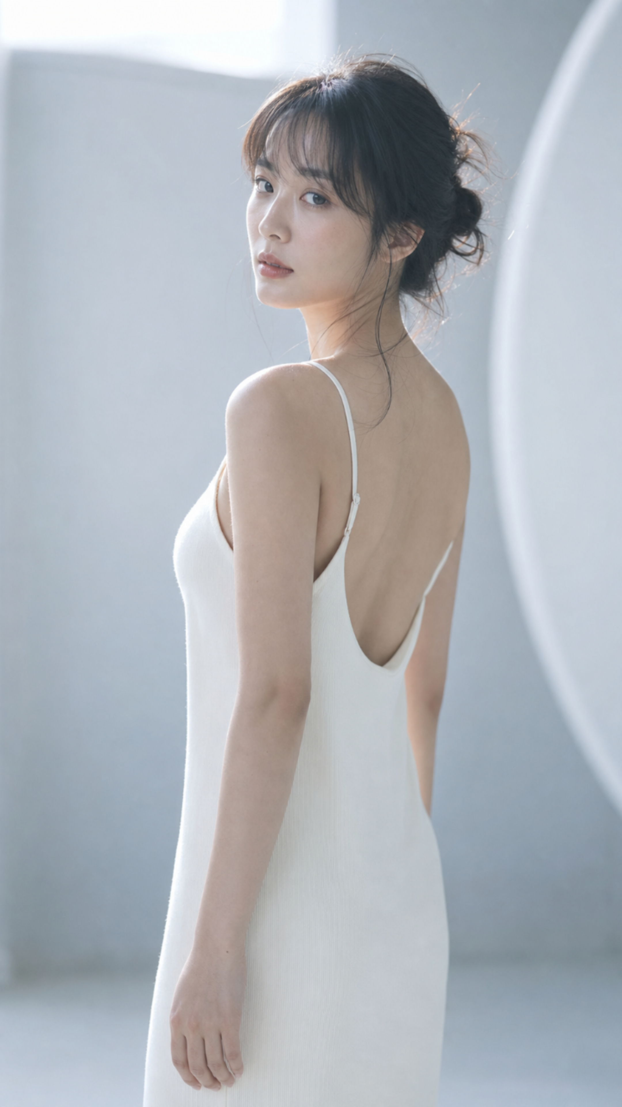 一位20多岁的年轻成年东亚女性站在浅冷灰色极简摄影棚或明亮室内空间中，画面从头顶